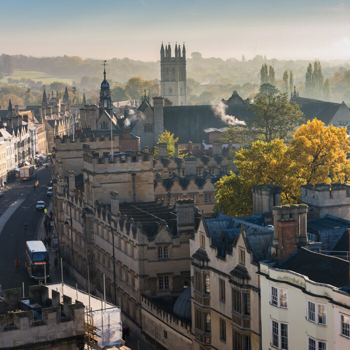 Aerial view of historic Oxford, England, showing old stone university buildings, Morrell Student Halls residence, yellow autumn trees, and rising morning mist under a hazy sky.