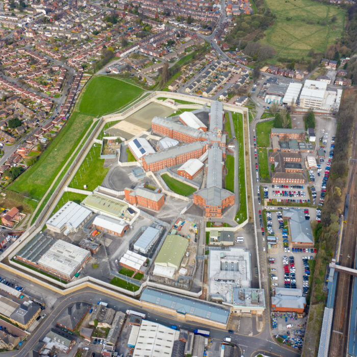 Aerial view of a large custodial facility with red and white buildings, surrounded by walls and green areas, set amid residential neighborhoods, roads, and parking lots.