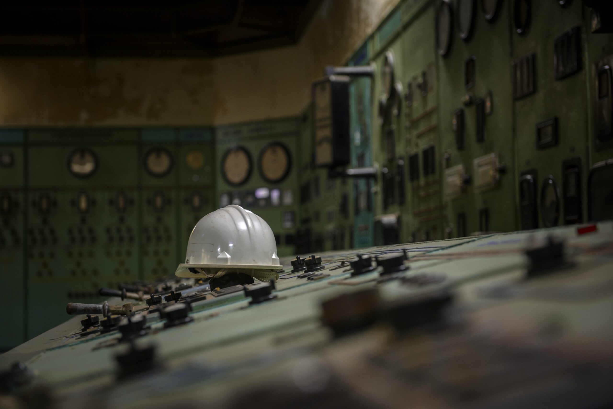 A white hard hat rests on top of an old control panel in a dimly lit room filled with vintage dials, switches, and gauges—capturing the industrial history valued by the Nuclear Institute’s Digital Special Interest Group.