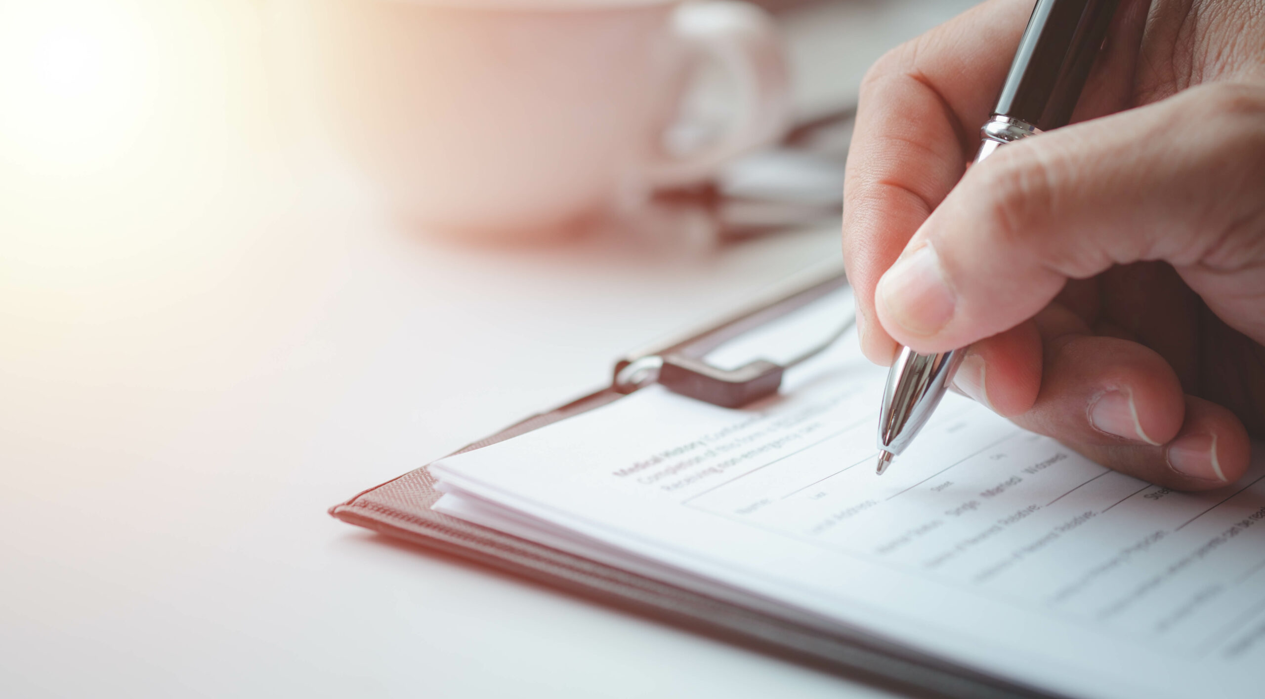 Close-up of a hand holding a pen and filling out a Building Inspection form on a clipboard, with a blurry coffee cup in the background.