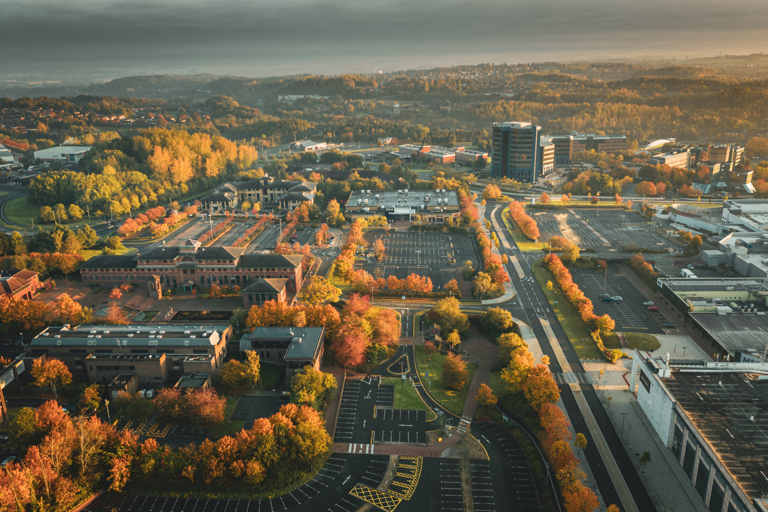 Aerial view of a cityscape in autumn, featuring colorful trees, parking lots, roads, office buildings, and distant hills under a cloudy sky—capturing the vibrant setting of homes in Telford.