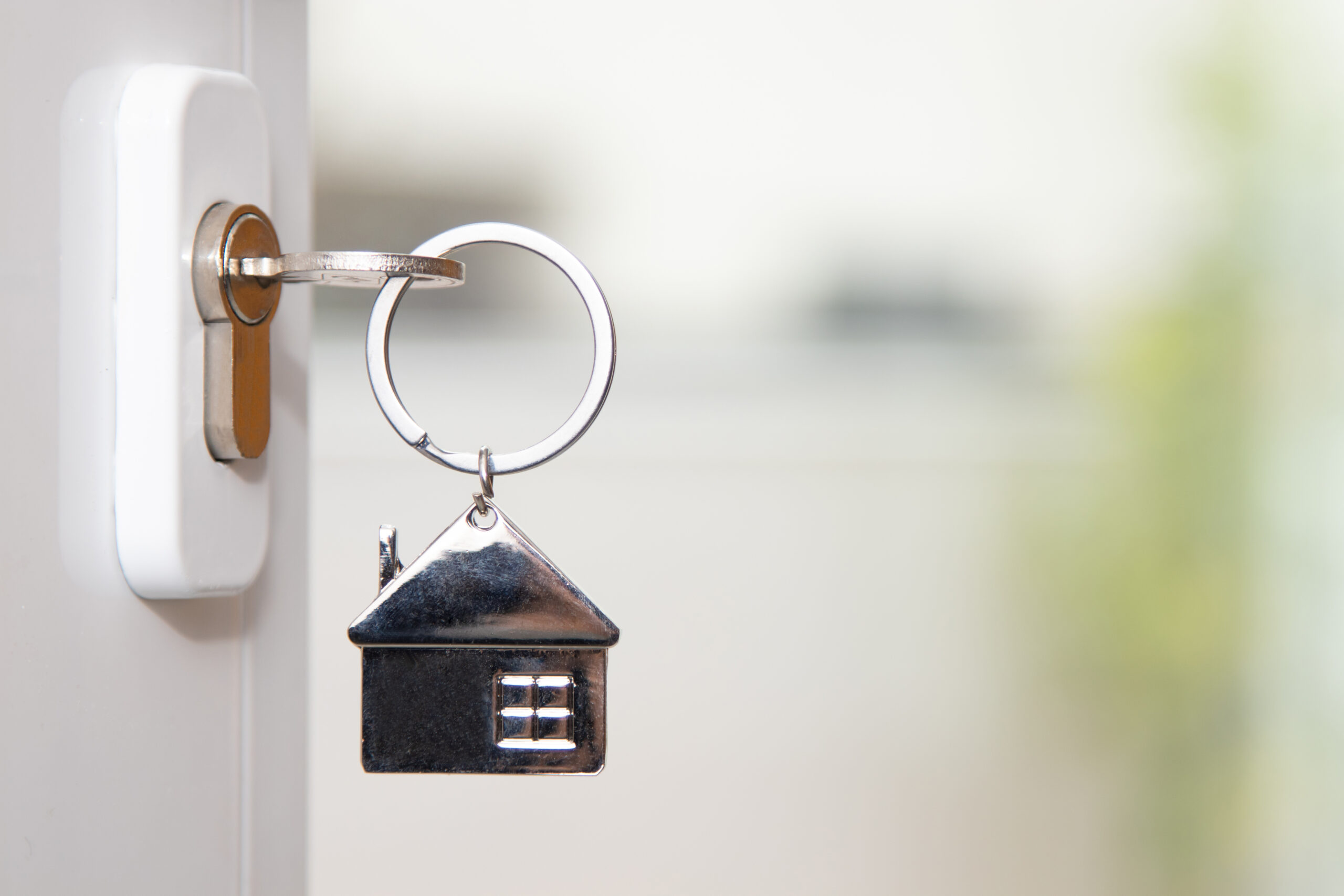 A silver key with a house-shaped keychain is inserted into a white door lock, symbolizing affordable housing opportunities in Coventry, with a blurred background.