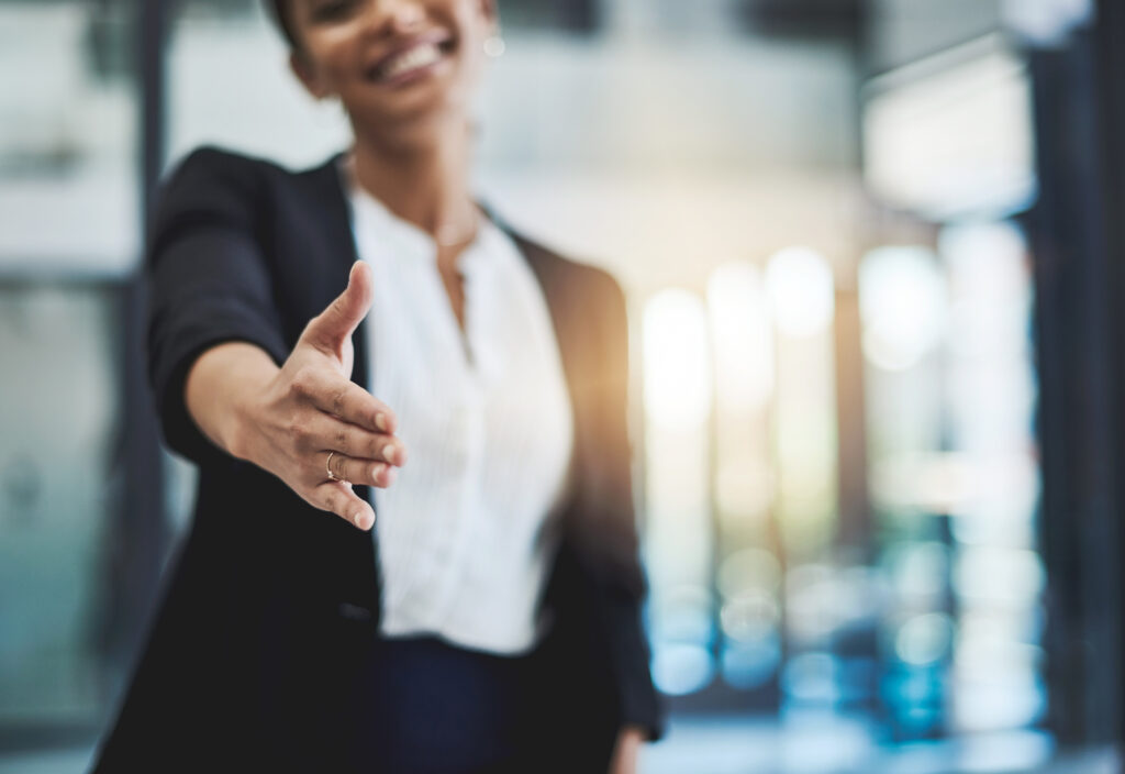 A smiling person in business attire extends their hand forward for a handshake, standing in Waldeck's bright, modern Sheffield Office.