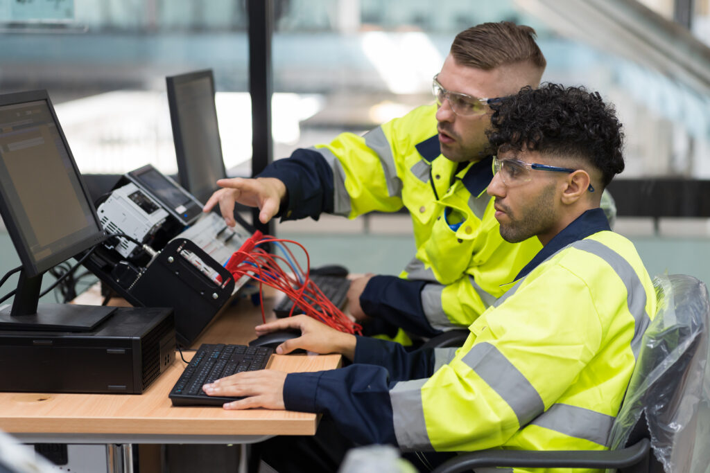 A group of men in safety gear, including Ben Preece, sit at a desk with computers, highlighting their teamwork during National Apprenticeship Week.