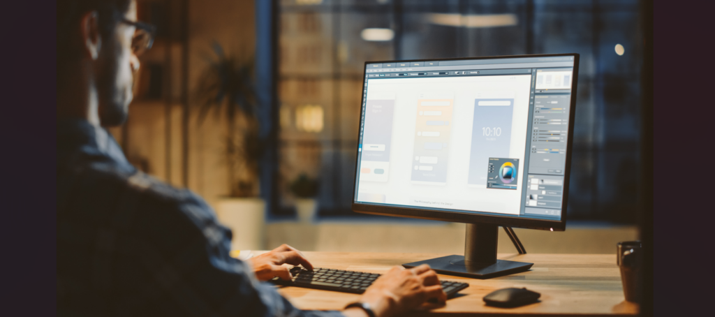 A person sits at a desk using a computer to design a mobile app interface, with design software and colorful UI elements displayed on the monitor in a modern, dimly lit office—exploring ways to invest in 360 virtual tour technology for 2023.