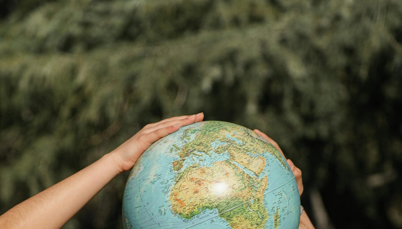 Four hands from two people hold up a globe outdoors amid green trees, symbolizing unity and care for the Earth—reminding us of the importance of Environmental Due Diligence in protecting our planet while building sustainable infrastructure.