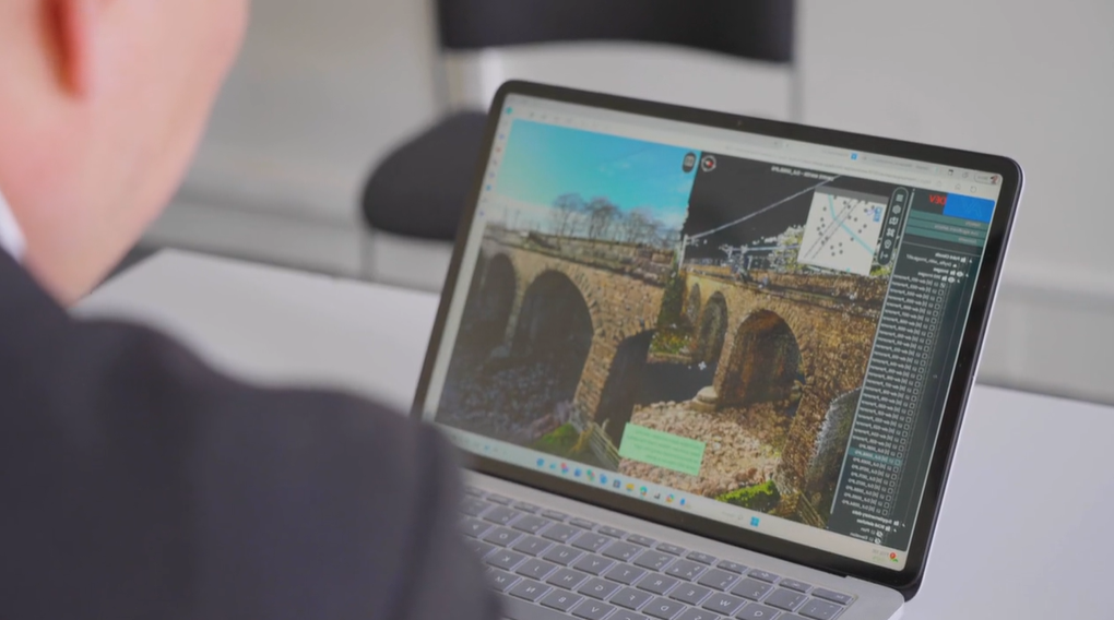 A person using a laptop displaying a detailed 3D digital model of a stone bridge, with various tools and menus visible on the screen to support Network Rail collaboration and integration.