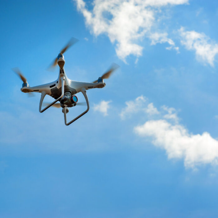 A white quadcopter drone equipped for asset inspection flies in a blue sky with scattered white clouds.