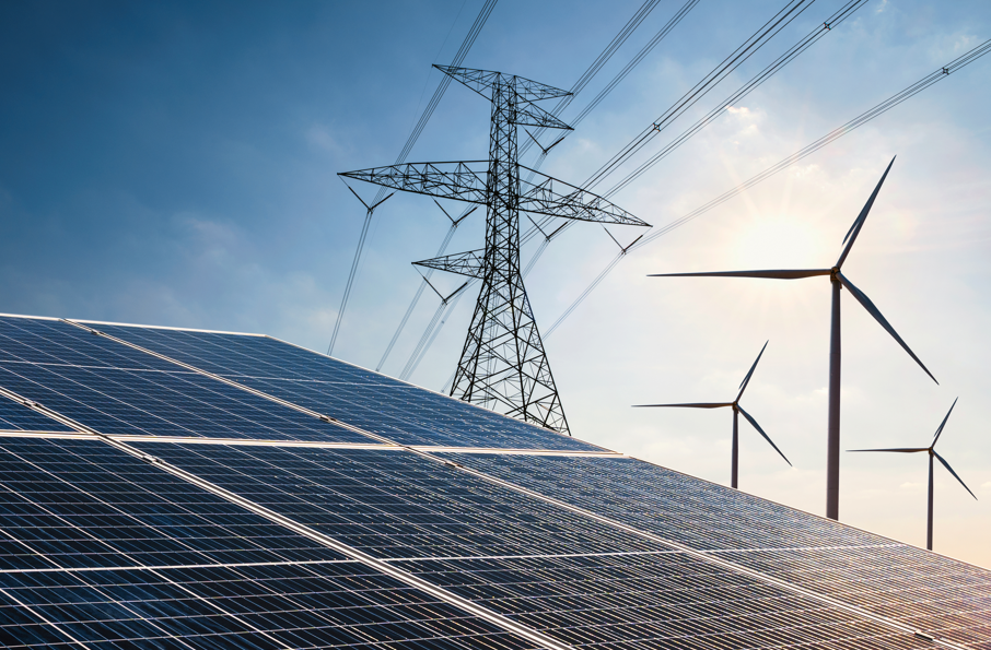 Solar panels in the foreground, with wind turbines and an electricity transmission tower in the background under a bright, partly cloudy sky—an ideal setting for Business or ESG Consultants focused on renewable energy solutions.